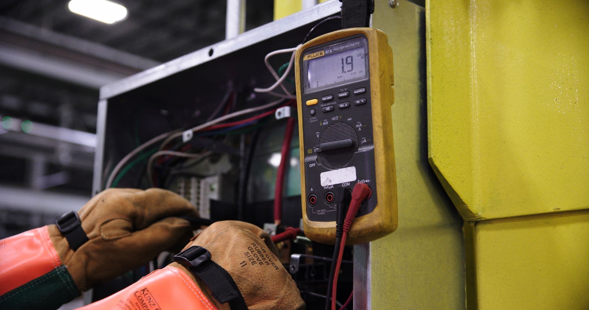 Electrician in insulated gloves testing a panel with a multimeter