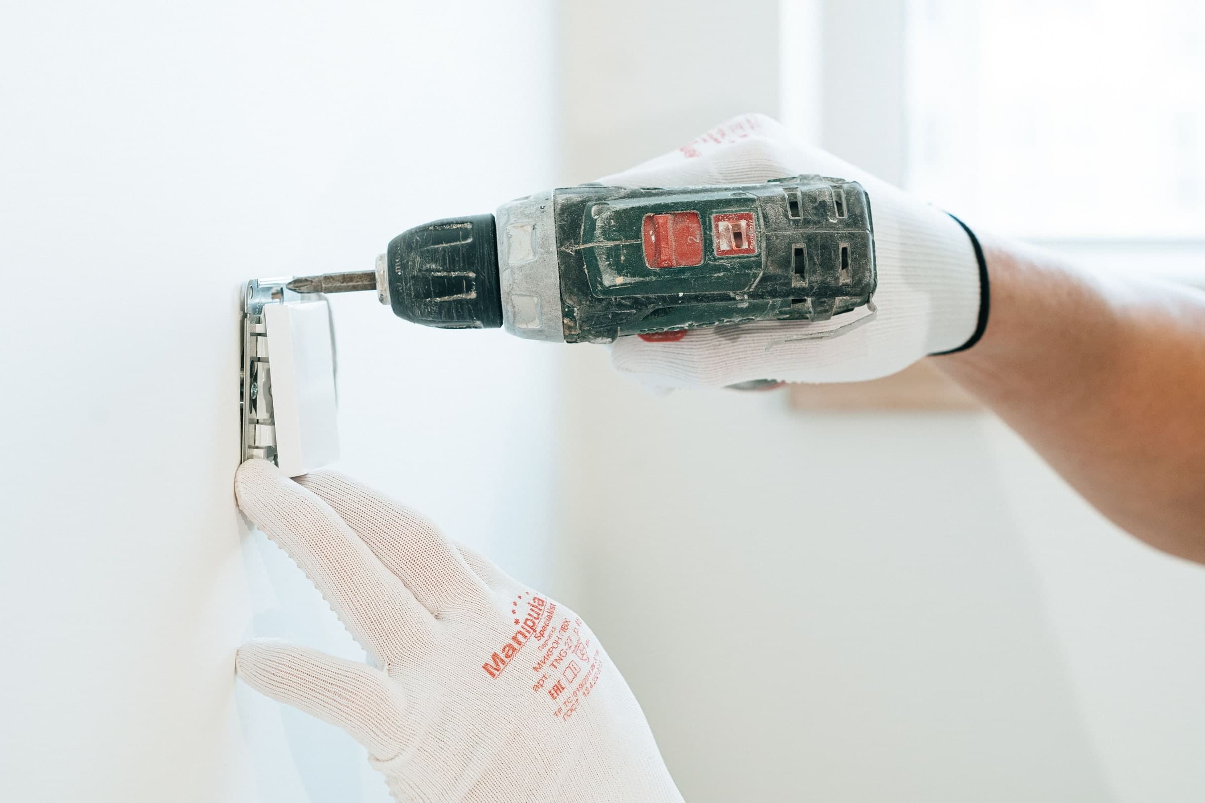 Electrician in work gloves fixing a new switch plate to a wall